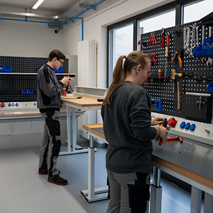 Zwei Mitarbeiter arbeiten an individuell eingerichteten Werkbänken in einer Werkstatt – ergonomische und anpassungsfähige Arbeitsplatzlösungen für die Elektroindustrie.