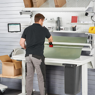 Mitarbeiter schneidet Verpackungsmaterial am Verpackungsarbeitsplatz mit Schneidgerät und Abrolleinheit – ideal für präzise Schnitte und effiziente Arbeitsabläufe.