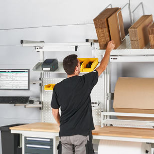 Mitarbeiter entnimmt Kartons aus einem Kartonagenmagazin an einem Verpackungsarbeitsplatz – ideal für effiziente Lagerung und schnellen Zugriff auf Verpackungsmaterial.